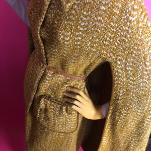 May include: A brown and white patterned cape with a brown leather belt and a zippered pocket. The cape has a collar and long sleeves.