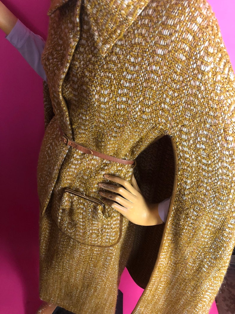 May include: A brown and white patterned cape with a brown leather belt and a zippered pocket. The cape has a collar and long sleeves.