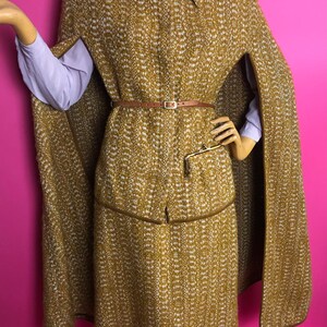 May include: A brown and white tweed cape and matching skirt with a brown leather belt. The cape has a collar and is lined with brown fabric. The skirt is knee-length and has a brown leather trim.