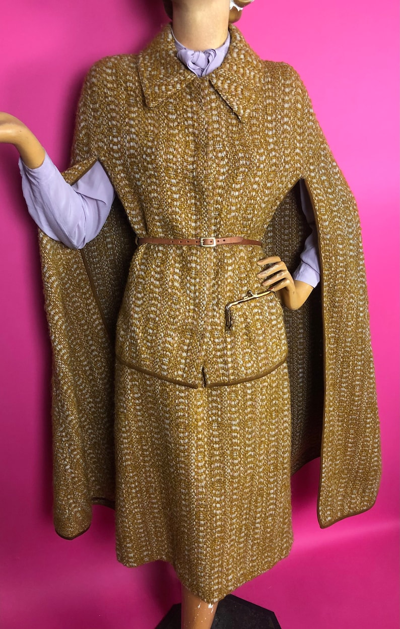 May include: A brown and white tweed cape and matching skirt with a brown leather belt. The cape has a collar and is lined with brown fabric. The skirt is knee-length and has a brown leather trim.