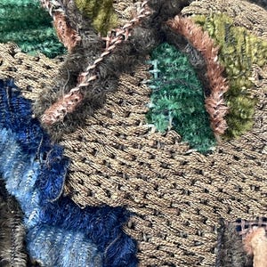 May include: Close-up of a textured fabric with a patchwork design. The fabric is made of different colors and textures, including brown, green, blue, and pink. The fabric is stitched together in a random pattern.