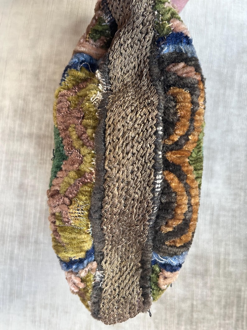 May include: A small, colorful, rectangular pouch with a brown fabric strap. The pouch is made of a variety of fabrics, including velvet, and has a patchwork design.