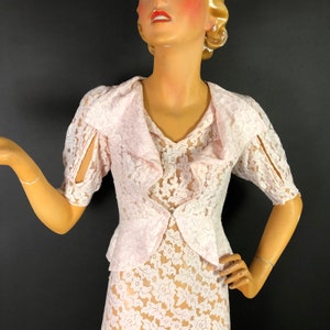 May include: A pink lace dress with a ruffled collar and short sleeves. The dress is made of delicate lace with a floral pattern.