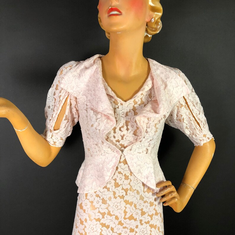 May include: A pink lace dress with a ruffled collar and short sleeves. The dress is made of delicate lace with a floral pattern.