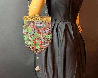 May include: A vintage, colorful, patterned, fabric evening bag with a gold metal frame and a dangling tassel. The bag has a long, brown cord strap.