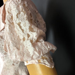 May include: A close-up of a pale pink lace fabric with a floral pattern. The fabric is gathered and ruffled, creating a soft and delicate look.