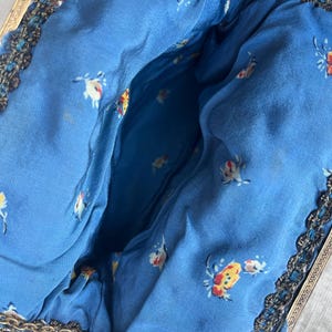 May include: A vintage beaded purse with a blue floral lining and a gold metal frame. The purse has a chain strap.