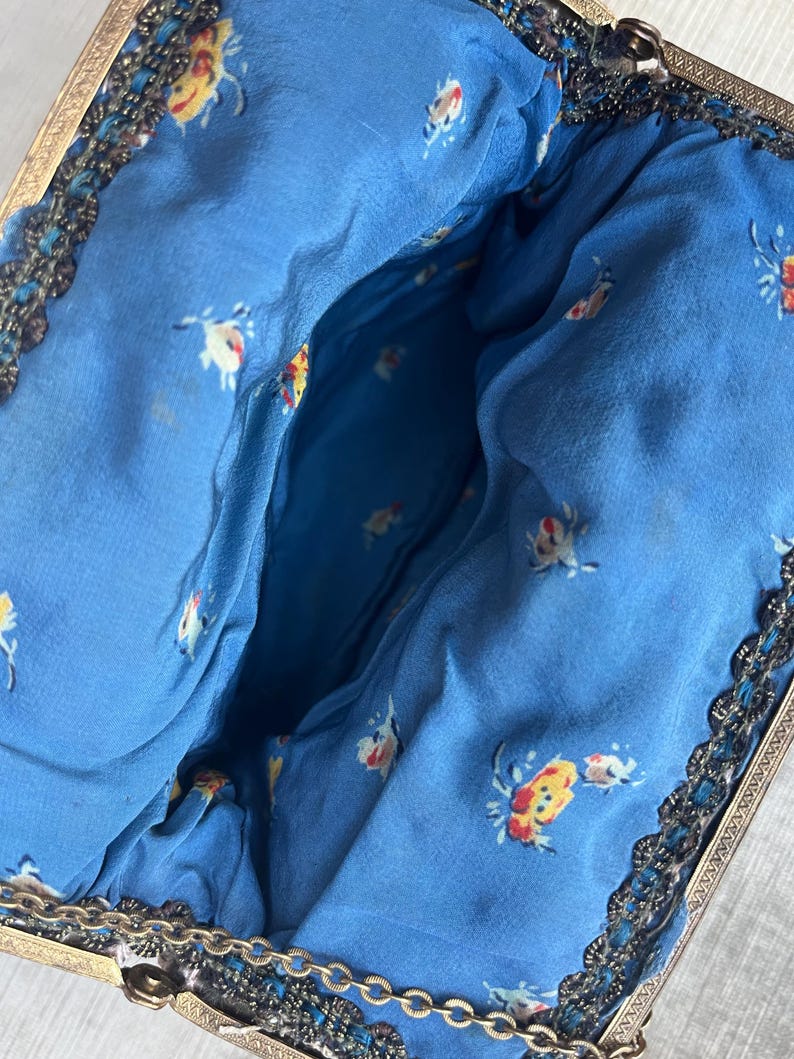 May include: A vintage beaded purse with a blue floral lining and a gold metal frame. The purse has a chain strap.