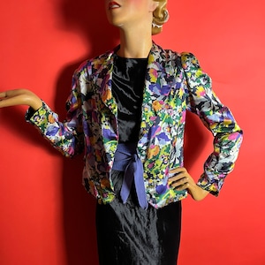 Puede incluir: Una chaqueta de estampado floral con una faja morada. La chaqueta tiene un fondo negro con flores rosas, amarillas, verdes y azules.