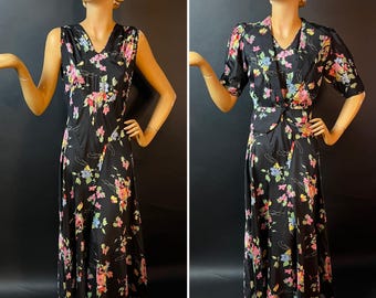 Vestido negro sin mangas con corte al bies y estampado floral de los años 30, con chaqueta de manga corta a juego, detalle acolchado en las solapas y mangas abullonadas.