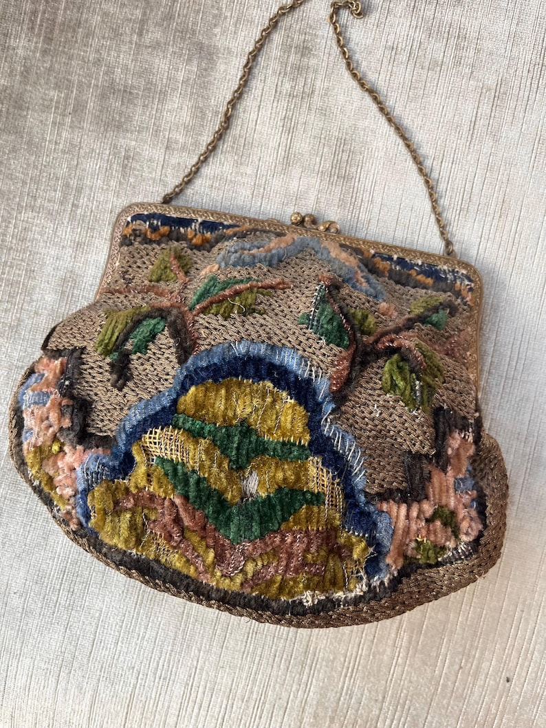 May include: A vintage embroidered purse with a chain strap. The purse is made of a brown fabric with colorful embroidery, including green, blue, yellow, and pink.