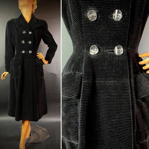 Puede incluir: Un abrigo de terciopelo negro con cierre de doble botonadura y bolsillos grandes. El abrigo tiene una cintura ajustada y una falda acampanada. Los botones son plateados y tienen un diseño en relieve.