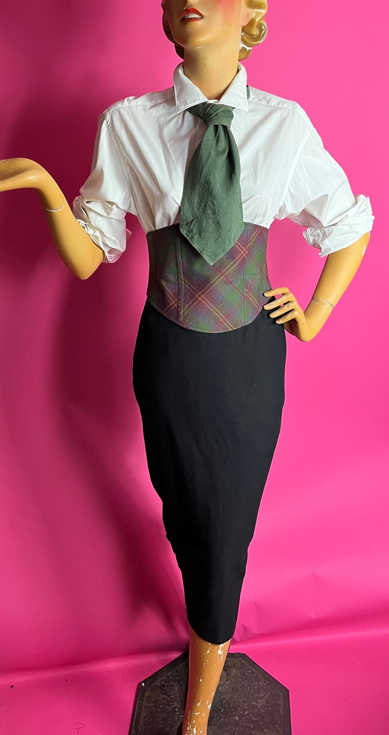 May include: A white button-down shirt with a green tie, a plaid corset, and a black pencil skirt.