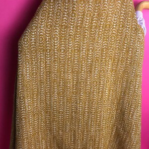 May include: A mustard yellow and white patterned cape with a brown trim. The cape is made of a soft, woven fabric.