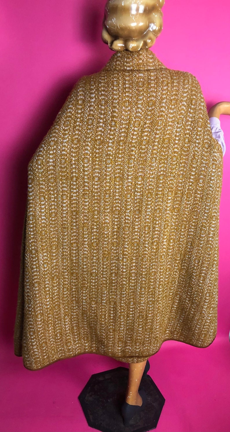 May include: A mustard yellow and white patterned cape with a brown trim. The cape is made of a soft, woven fabric.
