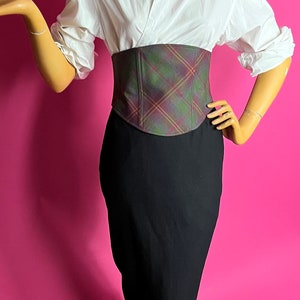 May include: A white button-down shirt with a plaid corset belt and a black pencil skirt.