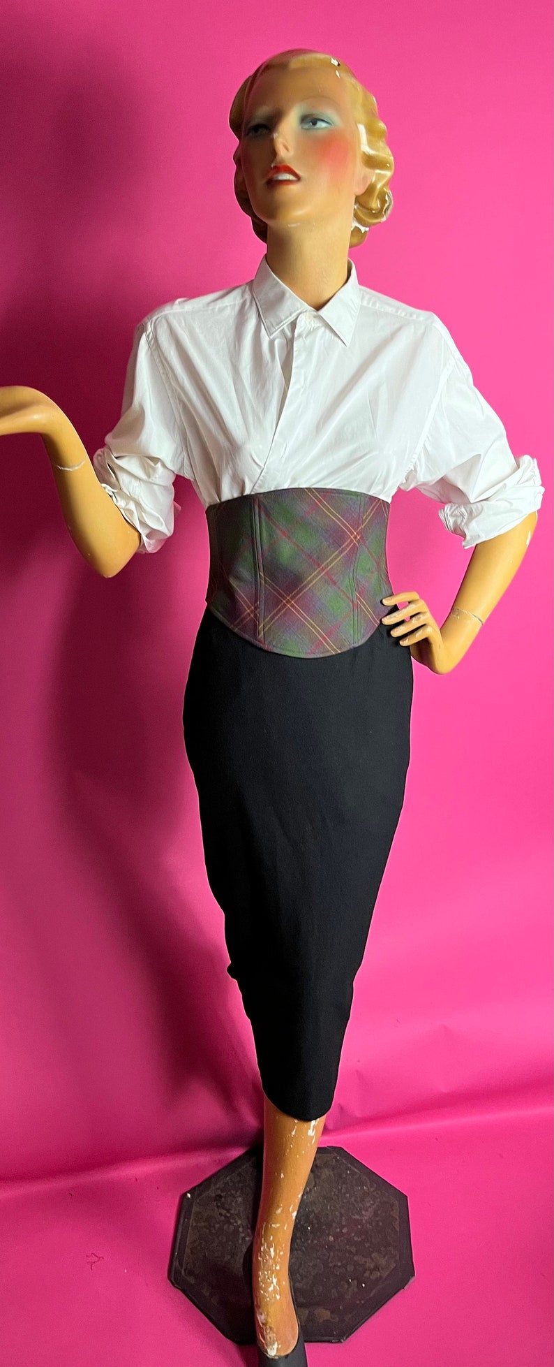May include: A white button-down shirt with a plaid corset belt and a black pencil skirt.