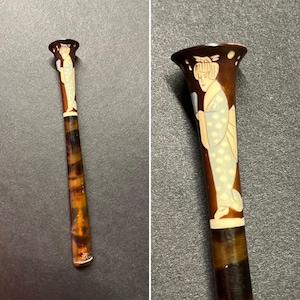 Puede incluir: Horquilla japonesa vintage con un diseño de geisha marrón y crema. La horquilla presenta una ilustración detallada de una geisha con kimono, sosteniendo un abanico. La horquilla mide aproximadamente 15 cm de largo.