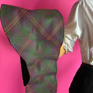 May include: A large, wide-brimmed hat made of a plaid fabric with green, purple, and brown tones. The hat is folded in half and has a curved shape.