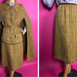 May include: A brown and white tweed skirt and matching cape with a brown leather belt. The skirt is knee-length and the cape has a collar.