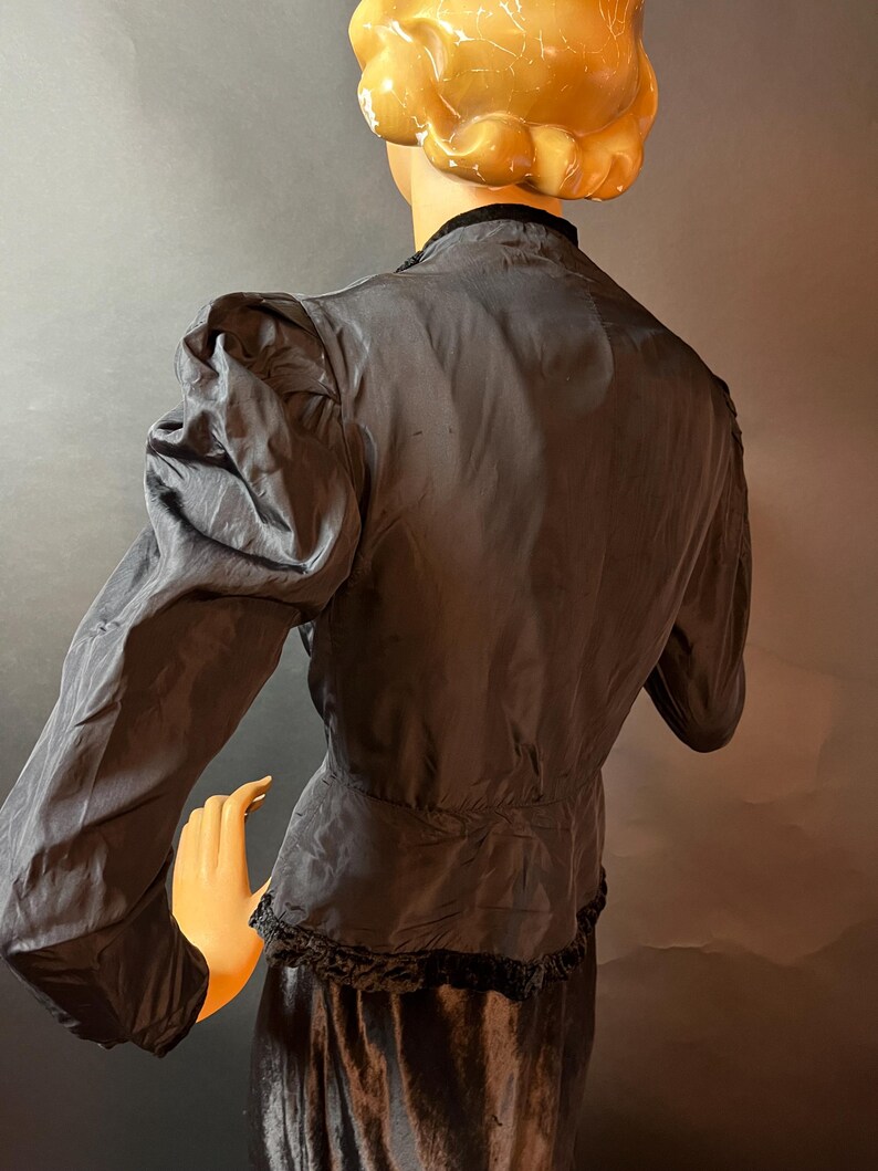 Op de afbeelding: Een zwart fluwelen jasje met een kantversiering en pofmouwen. Het jasje is getailleerd en heeft een getailleerde taille.