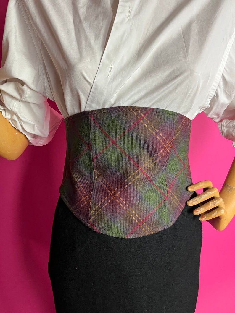 May include: A plaid corset with a green, brown, and red pattern. The corset is made of a soft, woven fabric and has a fitted silhouette.