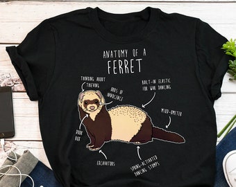 May include: A black t-shirt with a white illustration of a ferret and the text "Anatomy of a Ferret". The illustration shows different parts of the ferret labeled with humorous descriptions, such as "Orbs of Innocence", "Built-in Elastic for War Dancing", and "Spring-Activated Dancing Stumps".