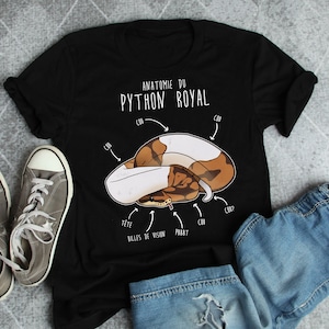 Könnte beinhalten: Schwarzes T-Shirt mit einer weißen Grafik einer Schlange mit dem Text "Anatomie du Python Royal" und Beschriftungen in Französisch für verschiedene Körperteile der Schlange.