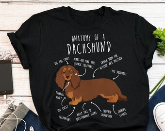 May include: Black t-shirt with a white graphic of a dachshund dog. The graphic includes text that says "Anatomy of a Dachshund" and labels different parts of the dog's body.