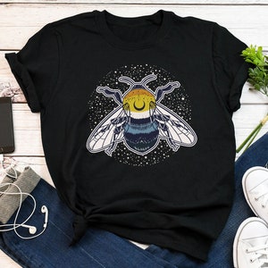May include: Black t-shirt featuring a graphic of a bee with a crescent moon on its head, surrounded by stars. The bee is yellow, black, and blue.