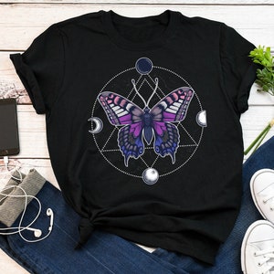 Könnte beinhalten: Schwarzes T-Shirt mit einem Motiv eines lila und pinkfarbenen Schmetterlings in einem geometrischen Kreis mit Monden und Sternen.