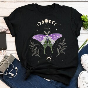 Może przedstawiać: Czarny T-shirt z grafiką fioletowego i zielonego motyla, otoczonego rogalem księżyca, gwiazdami i geometrycznym wzorem.