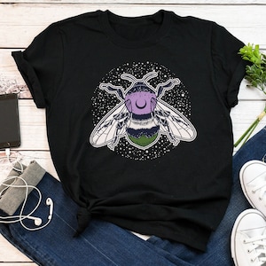 May include: Black t-shirt featuring a graphic of a purple and green bee with a crescent moon on its head, surrounded by white stars.