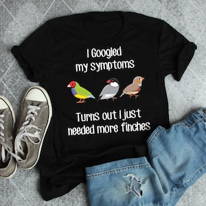 May include: Black t-shirt with the text "I Googled my symptoms, Turns out I just needed more finches." The shirt features three cartoon finches in various colours. Grey canvas trainers and blue denim shorts are also visible.