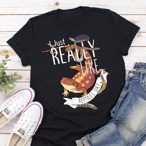 Peut inclure: T-shirt noir avec un graphique d'un dragon barbu, d'un serpent, d'une tortue et d'un gecko. Le texte sur le t-shirt est "J'aime vraiment les reptiles, ok?"