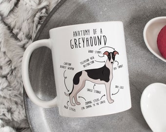 Może przedstawiać: Biały ceramiczny kubek z czarno-białym rysunkiem psa rasy chart. Rysunek jest opisany humorystycznymi terminami anatomicznymi, takimi jak "worry stamps", "telewizyjny widok przeszkody" i "przechowywanie przekąsek".