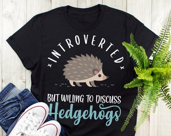 Könnte beinhalten: Schwarzes T-Shirt mit dem Text "Introvertiert, aber bereit, über Igel zu diskutieren" in Weiß. Ein Cartoon-Igel befindet sich über dem Text.