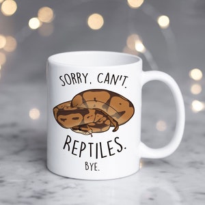 Puede incluir: Taza de cerámica blanca con una ilustración de serpiente marrón y beige. La taza tiene el texto "Lo siento, no puedo. Reptiles. Adiós." impreso en ella.