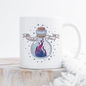 May include: White ceramic mug with a graphic of a glass bottle with a cork stopper and a flame inside. The bottle is surrounded by stars and a banner that reads "Soul Fire".