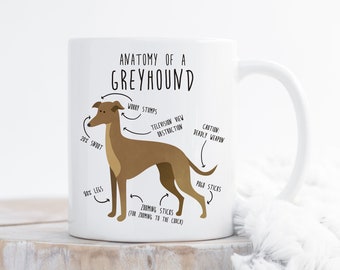 Może przedstawiać: Biały kubek ceramiczny z ilustracją brązowego psa rasy Greyhound w stylu kreskówkowym. Kubek zawiera humorystyczny schemat anatomiczny Greyhunda z etykietami takimi jak "Zoomie Sticks" i "Śmiertelna broń".