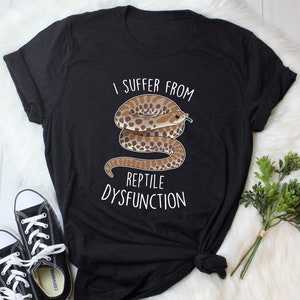 Puede incluir: Camiseta negra con un gráfico blanco de una serpiente y el texto "I suffer from reptile dysfunction".