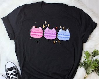 May include: Black t-shirt with a graphic of three pastel-colored cat macarons with glitter accents.