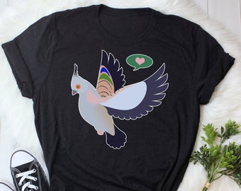 Könnte beinhalten: Schwarzes T-Shirt mit einer Cartoon-Illustration eines grau-weißen Vogels mit einer grünen Sprechblase, die ein rosa Herz enthält. Der Vogel hat einen regenbogenfarbenen Schwanz.