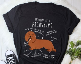 May include: A black t-shirt with a white graphic of a dachshund dog. The graphic includes text that says "Anatomy of a Dachshund" and labels different parts of the dog's body.