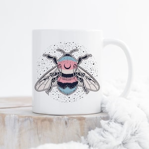 May include: White ceramic mug with a black and white illustration of a bee with a crescent moon on its head. The bee is surrounded by a circle of stars.