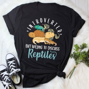 May include: Black t-shirt with a graphic of a chameleon, snake, turtle, and lizard. The text reads "Introverted but willing to discuss Reptiles".