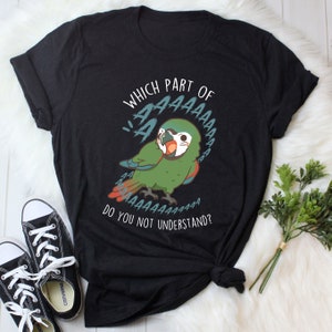 Puede incluir: Camiseta negra con una ilustración de un loro verde y azul. El loro dice "AAAAAAA" en un globo de diálogo. El texto debajo del loro dice "¿Qué parte de 'AAAAAAA' no entiendes?"