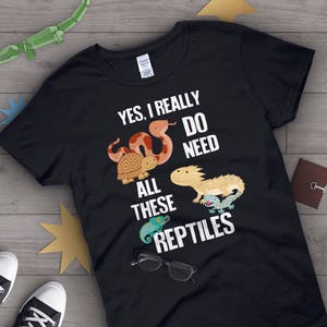 May include: Black t-shirt with white text that reads "Yes, I really do need all these reptiles". The shirt features a cartoon image of a snake, turtle, lizard, and chameleon.