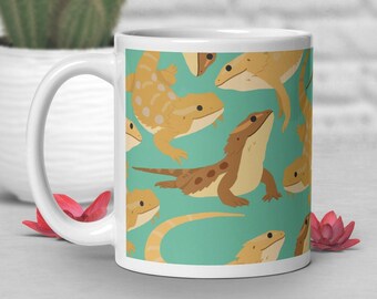 Puede incluir: Taza de cerámica blanca con fondo azul verdoso y un patrón repetido de dragones barbudos marrones y amarillos.