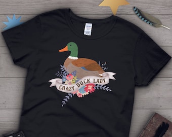 Puede incluir: Camiseta negra con un gráfico de un pato con flores y el texto "Crazy Duck Lady".